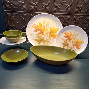 May include: A set of four green and white vintage dishes. The set includes a large oval serving bowl, a small bowl, a cup and saucer, and two dinner plates with a leaf design.