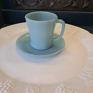 May include: A light blue glass teacup and saucer set. The cup has a handle and the saucer has a scalloped edge.