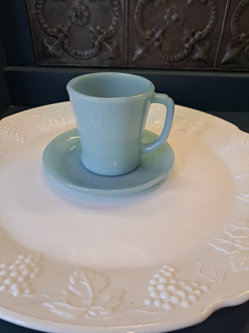 May include: A light blue glass teacup and saucer set. The cup has a handle and the saucer has a scalloped edge.