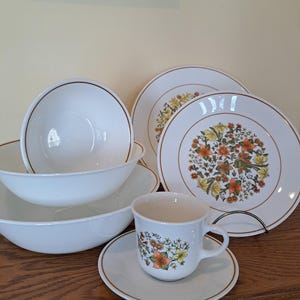 May include: A set of white Corelle dinnerware with a floral pattern in shades of orange, yellow, and green. The set includes a bowl, a plate, a cup, and a saucer.
