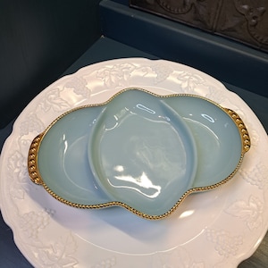May include: A light blue glass serving dish with three sections and a gold rim. The dish is sitting on a white plate with a grapevine design.