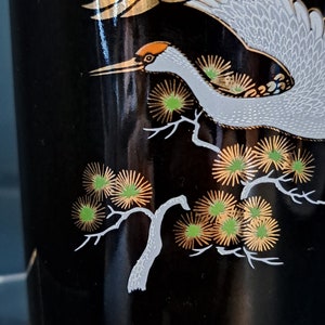 May include: Black ceramic vase with a white crane flying over a gold and green stylized pine tree design.