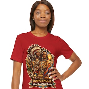 Pode incluir: Camiseta vermelha com um gráfico de duas pessoas em trajes tradicionais nativos americanos. O gráfico oval inclui o texto "INDIGENOUS BLACK AMERICANS" em uma faixa. A camiseta está sendo usada por uma pessoa. A imagem está bem iluminada.