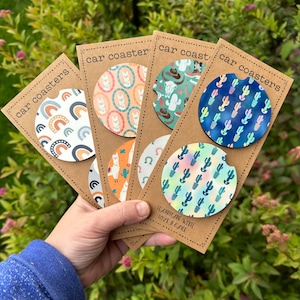 May include: Set of six car coasters with various designs. The coasters feature a rainbow, llama, cactus, and cowboy boot patterns. The coasters are handmade with love and care.
