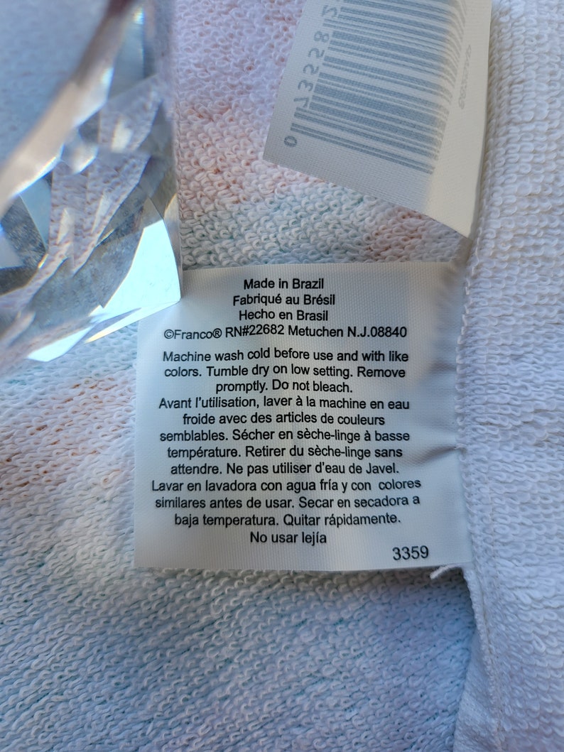 May include: White care label with black text detailing washing instructions for a garment. The label reads "Made in Brazil, Fabriqu&eacute; au Br&eacute;sil, Hecho en Brasil, &copy;Franco&reg; RN#22682 Metuchen N.J.08840, Machine wash cold before use and with like colors. Tumble dry on low setting. Remove promptly. Do not bleach. Avant l'utilisation, laver &agrave; la machine en eau froide avec des articles de couleurs semblables. S&eacute;cher en s&egrave;che-linge &agrave; basse temp&eacute;rature. Retirer du s&egrave;che-linge sans attendre. Ne pas utiliser d'eau de Javel. Lavar en lavadora con agua fr&iacute;a y con colores similares antes de usar. Secar en secadora a baja temperatura. Quitar r&aacute;pidamente. No usar lej&iacute;a, 3359".