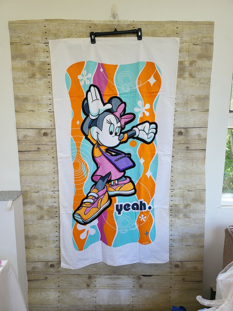 May include: A white beach towel with a colorful retro design featuring a cartoon Minnie Mouse wearing sneakers and a purple bag. The text "yeah." is printed on the towel.