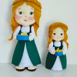 May include: Two felt dolls dressed in green dresses with white aprons and yellow hair. The dolls are holding blue bowls with yellow food inside.