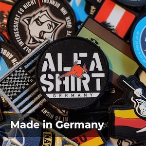 May include: A selection of embroidered patches with diverse designs and text. The central patch is black with white text reading "ALFA SHIRT GERMANY" and a red fish logo. Other patches feature a wolf, flags, and various text.