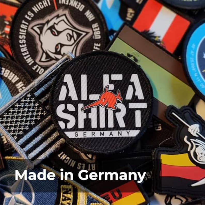May include: A selection of embroidered patches with diverse designs and text. The central patch is black with white text reading "ALFA SHIRT GERMANY" and a red fish logo. Other patches feature a wolf, flags, and various text.