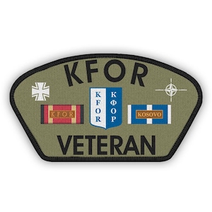 Può includere: Toppa da veterano KFOR verde oliva con bordo nero. Presenta la scritta "KFOR" sopra "VETERAN". Include una croce bianca, un nastro rosso e oro, un nastro blu e bianco e un simbolo NATO.
