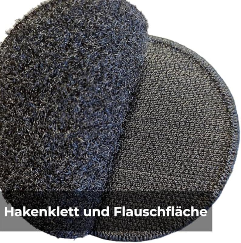 May include: Close-up of two dark grey circular hook-and-loop fastener pads. One pad has a fuzzy, textured surface, while the other has a more tightly woven, looped surface. The text "Hakenklett und Flauschfl&auml;che" is visible.