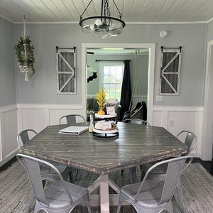 Puede incluir: Una mesa de comedor hexagonal de madera con una base blanca y sillas de metal gris. La mesa está decorada con una bandeja de tres niveles con una planta, un letrero que dice "need" y un letrero que dice "maybe". La mesa está puesta con un portátil y un cuaderno.