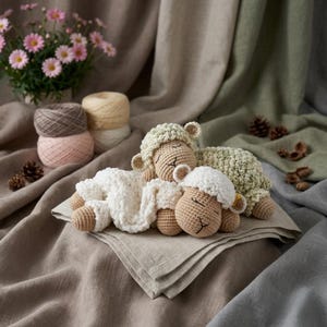 May include: Three crocheted sheep toys in cream, tan, and light green, resting on a linen napkin. The sheep have closed eyes and fluffy white wool. Yarn balls and a potted plant with pink flowers are in the background.