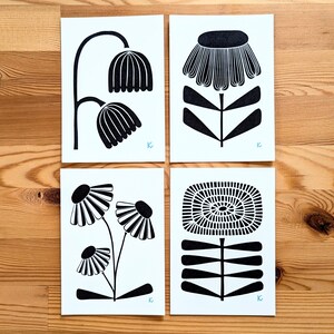 May include: Four black and white floral art prints. Each print features a different stylized flower design. The prints are on white paper and are arranged on a wooden surface. Each print has a small blue letter "K" in the corner.