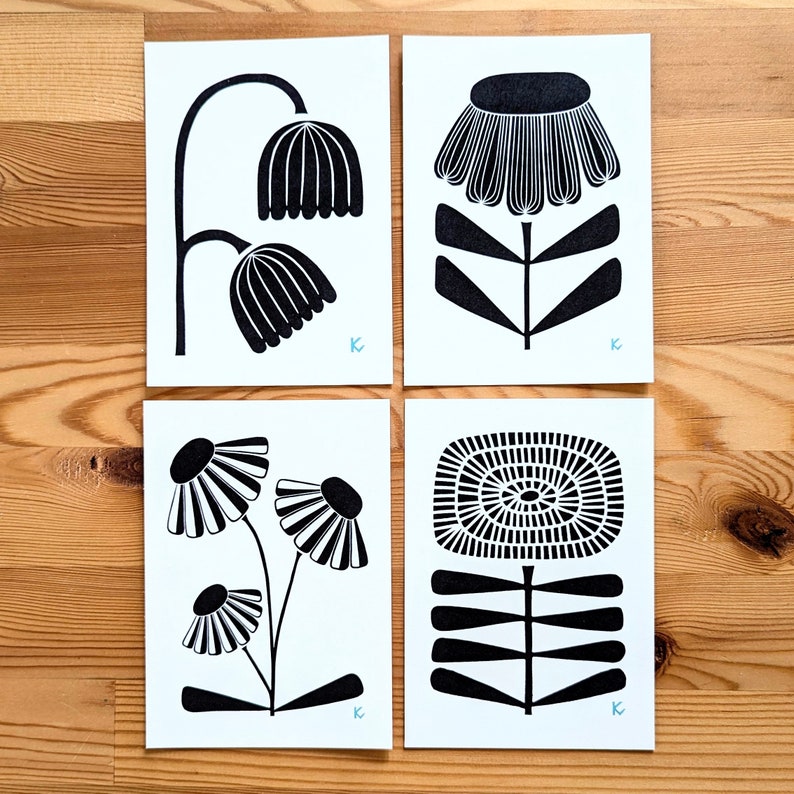 May include: Four black and white floral art prints. Each print features a different stylized flower design. The prints are on white paper and are arranged on a wooden surface. Each print has a small blue letter "K" in the corner.