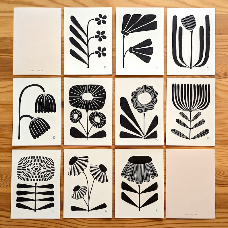 May include: A collection of twelve art prints featuring black and white floral designs. Each print showcases a unique stylized flower illustration on a white background. The prints are arranged on a wooden surface. The text "Linel und So" is visible on two of the prints.