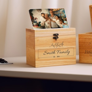 May include: Two wooden boxes with lids. The box on the left has a photo of a family on the lid and says "Smith Family Est. 2019". The box on the right has a floral design and says "Haley + Kyle December 12, 2019".