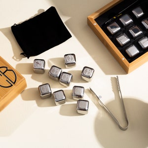 May include: A set of stainless steel whiskey stones in a wooden box with a black velvet pouch and tongs. The stones are engraved with the letter "B".