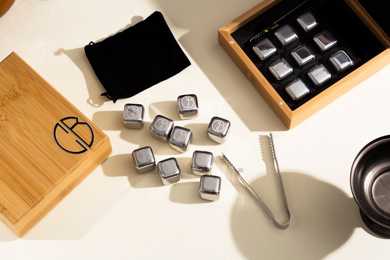 May include: A set of stainless steel whiskey stones in a wooden box with a black velvet pouch and tongs. The stones are engraved with the letter "B".