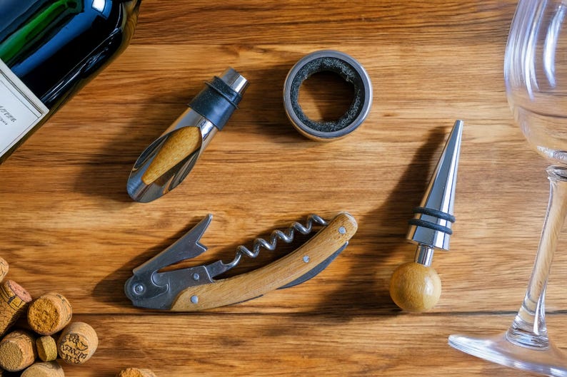 May include: A set of wine accessories including a corkscrew, a bottle stopper, a wine pourer, and a wine ring. The accessories are on a wooden surface.