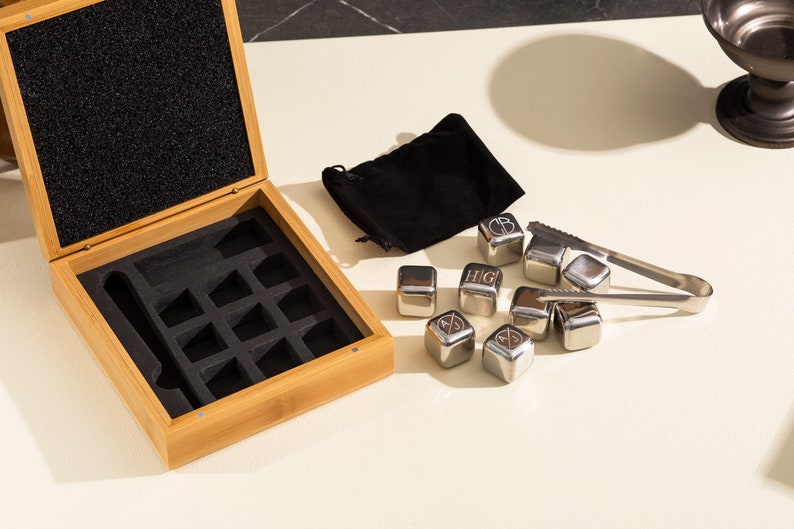May include: A set of eight stainless steel ice cubes with engraved letters and a black velvet pouch. The ice cubes are in a wooden box with a black foam interior. The box also includes a pair of tongs.