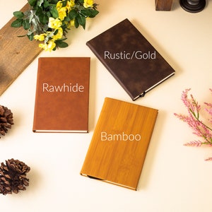 May include: Three closed notebooks with different covers. The covers are brown leather with the text "Rawhide", brown leather with the text "Rustic/Gold", and a wood grain pattern with the text "Bamboo".