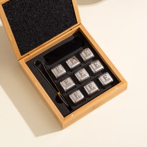 May include: A set of nine stainless steel whiskey stones in a wooden box with a pair of tongs. Each stone is engraved with the letter "E".