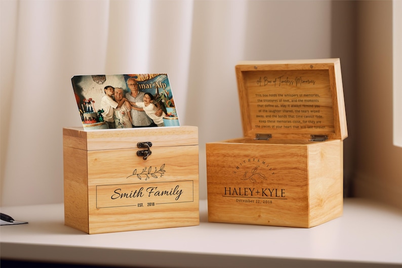 May include: Two wooden boxes with personalized engravings. The box on the left has a photo of a family on top and says "Smith Family Est. 2018". The box on the right says "Haley + Kyle December 12, 2018" and has a quote about a box of treasured memories.