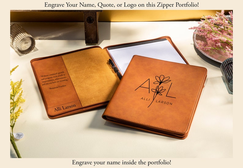 May include: Tan leather zipper portfolio with a personalized floral design and the initials "A L". The portfolio is open, revealing a notepad and pen. The text "Engrave Your Name, Quote, or Logo on this Zipper Portfolio!" is at the top.