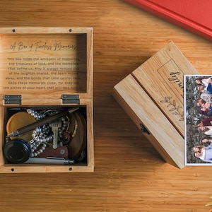 May include: A wooden box with a hinged lid, engraved with the text "A Box of Timeless Memories". The inside of the box is lined with felt and contains a variety of small items, including a necklace, a key, and a pen. The box is sitting on a wooden surface.