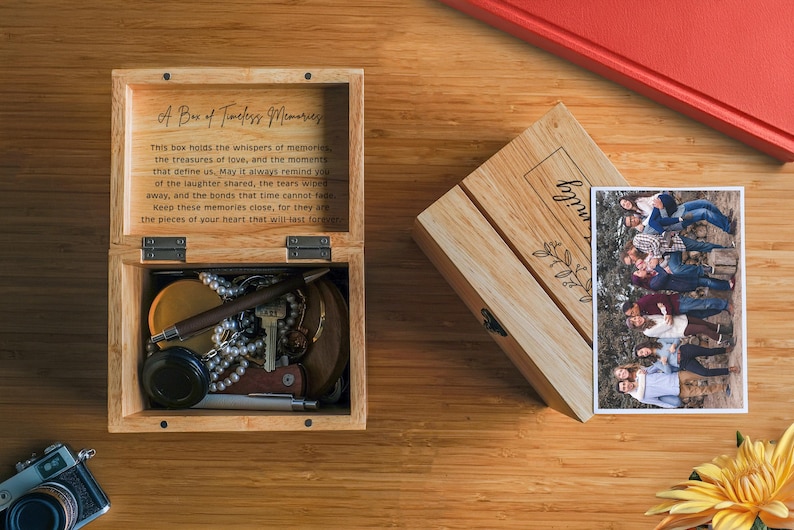 May include: A wooden box with a hinged lid, engraved with the text "A Box of Timeless Memories". The inside of the box is lined with felt and contains a variety of small items, including a necklace, a key, and a pen. The box is sitting on a wooden surface.