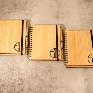 May include: Three bamboo notebooks with black elastic bands and matching pens. Each notebook has a different monogram engraved on the front.