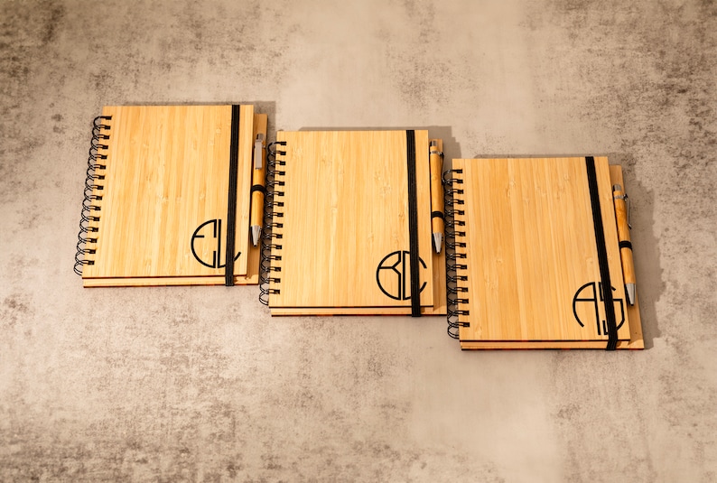 May include: Three bamboo notebooks with black elastic bands and matching pens. Each notebook has a different monogram engraved on the front.