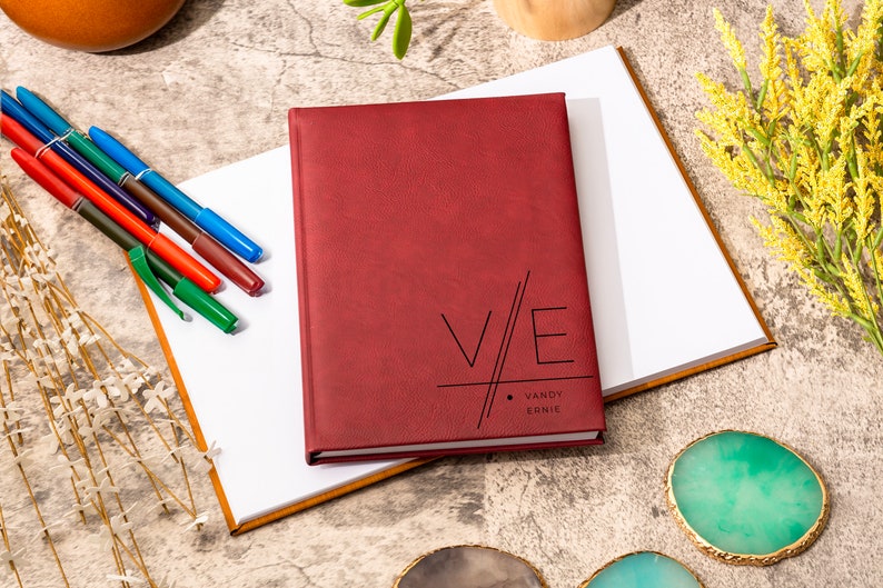 May include: A burgundy leather-bound journal with the initials "V/E" and the names "Vandy Ernie" printed in black on the front cover.