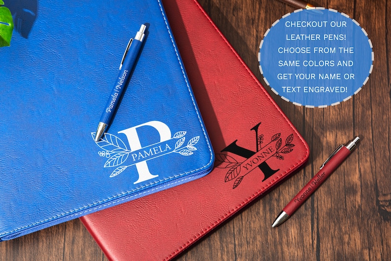 May include: Blue and red leather journals with personalized initials and names, accompanied by matching pens. The blue journal features the initial "P" and the name "Pamela", while the red journal displays "Yvonne". The pens are also engraved.