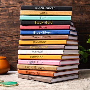 May include: A stack of 15 notebooks with different colored covers. The covers are labeled with the following colors: Black-Silver, Cork, Teal, Black-Gold, Rose, Blue-Silver, Dark Brown, Bamboo, Rustic-Gold, Marble, Bamboo, Light Pink, Light Brown, Rawhide, and Gray.