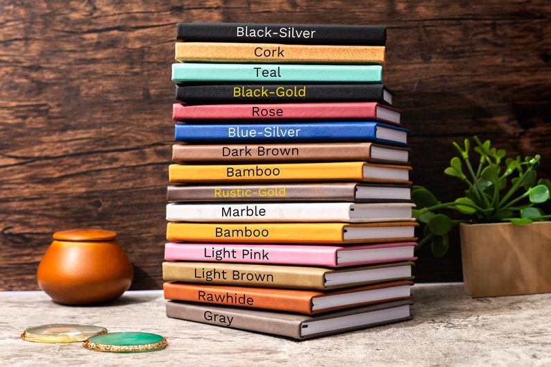 May include: A stack of 15 notebooks with different colored covers. The covers are labeled with the following colors: Black-Silver, Cork, Teal, Black-Gold, Rose, Blue-Silver, Dark Brown, Bamboo, Rustic-Gold, Marble, Bamboo, Light Pink, Light Brown, Rawhide, and Gray.