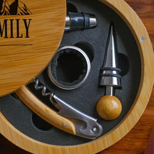 May include: A wooden box with a lid that opens to reveal a wine opener set. The set includes a corkscrew, a bottle stopper, a pourer, and a foil cutter. The box is engraved with the text "With Family Since 2025".