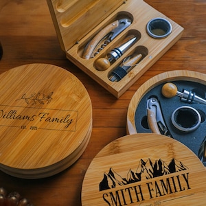 May include: Two personalised bamboo wine bottle opener sets. One set features a mountain design with the text "Smith Family Est. 2025". The other set features a floral design with the text "Williams Family Est. 2025".