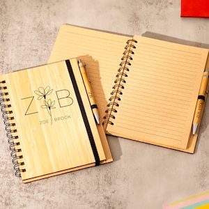 May include: A bamboo notebook with a black elastic closure and a matching pen. The notebook has a personalized design with the initials "Z & B" and the names "Zoe Brook".