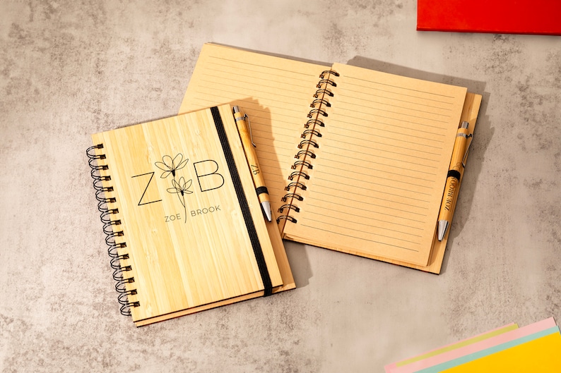 May include: A bamboo notebook with a black elastic closure and a matching pen. The notebook has a personalized design with the initials "Z & B" and the names "Zoe Brook".