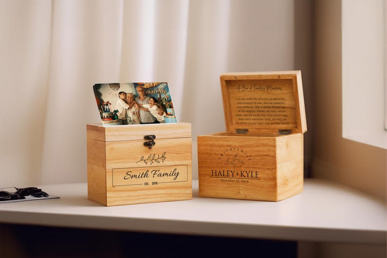 May include: Two wooden boxes with lids. The box on the left has a photo of a family on the lid and says "Smith Family Est. 2019". The box on the right has a floral design and says "Haley + Kyle December 12, 2019".