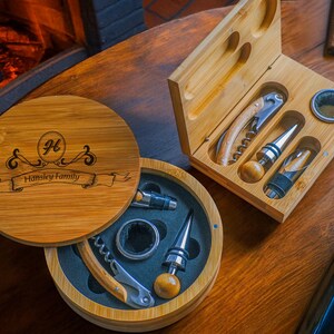 May include: A wooden box with a personalised inscription, "H.  Hinsley Family", containing a wine opener, bottle stopper, and other wine accessories. The box is open and the accessories are visible.