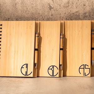 May include: Three wooden notebooks with spiral binding and matching pens. Each notebook has a different monogram in a circle: EL, BC, and AS.