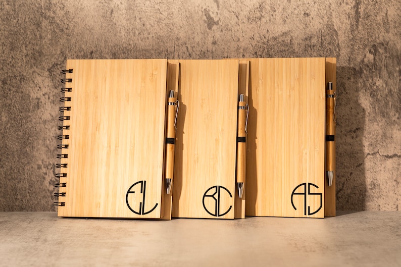May include: Three wooden notebooks with spiral binding and matching pens. Each notebook has a different monogram in a circle: EL, BC, and AS.