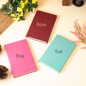 May include: Three closed notebooks with different colored covers: pink, teal, and burgundy. The covers are labeled "Pink", "Teal", and "Rose".
