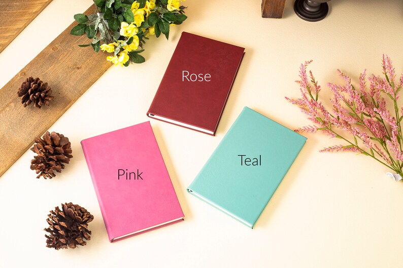 May include: Three closed notebooks with different colored covers: pink, teal, and burgundy. The covers are labeled "Pink", "Teal", and "Rose".