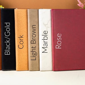 May include: A collection of six leather-bound journals in various colors: Rawhide, Black/Gold, Cork, Light Brown, Marble, and Rose. Each journal has a different texture and color, with the names of the colors printed vertically on the spine.