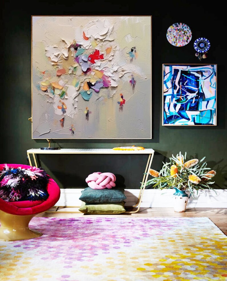 K&ouml;nnte beinhalten: Ein Wohnzimmer-Interieur mit einem farbenfrohen abstrakten Gem&auml;lde, einem modernen Sessel und einem gemusterten Teppich. Das Gem&auml;lde zeigt einen strukturierten, wei&szlig;en Hintergrund mit bunten abstrakten Formen und Figuren. Der Sessel ist leuchtend pink mit einem schwarz-wei&szlig;en flauschigen Kissen. Der Teppich ist ein mehrfarbiger, abstrakter Entwurf in Pink-, Gelb- und Wei&szlig;t&ouml;nen.