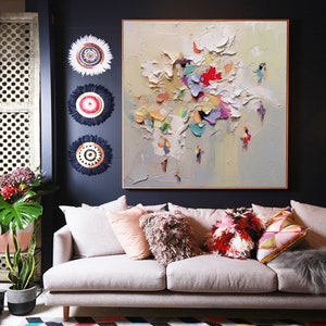 K&ouml;nnte beinhalten: Ein wei&szlig;es Sofa mit bunten Kissen steht vor einer dunkelblauen Wand mit einem gro&szlig;en abstrakten Gem&auml;lde und drei dekorativen Wandbeh&auml;ngen. Ein bunter geometrischer Teppich bedeckt den Boden.